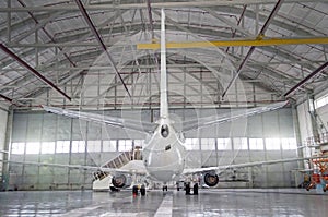 Passenger aircraft on maintenance of engine and fuselage repair in airport hangar. Rear view of the tail.