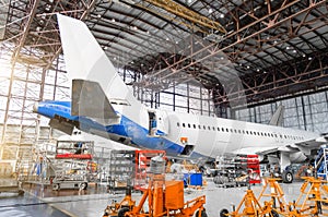 Passenger aircraft on maintenance of engine repair, among the jacks, a view of the tail and the rear of the fuselage in airport ha