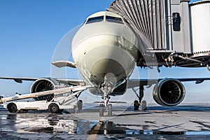 The passenger aircraft stands at the boarding bridge on an airport apron. The baggage compartment of the airplane is open and the