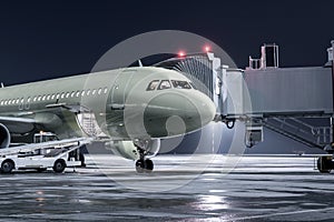 The passenger aircraft stands at the jetway on an airport night apron. The baggage compartment of the airplane is open and the