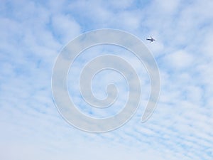 The passenger airplane is flying far away in the blue sky and white clouds. Aircraft in the air. Light background or backdrop