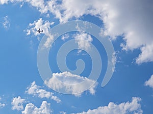 The passenger airplane is flying far away in the blue sky and white clouds. Aircraft in the air. Light background or backdrop