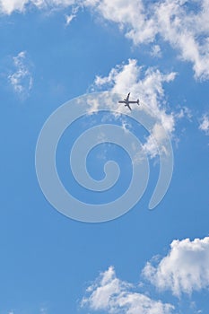 The passenger airplane is flying far away in the blue sky and white clouds. Aircraft in the air. Light vertical background or