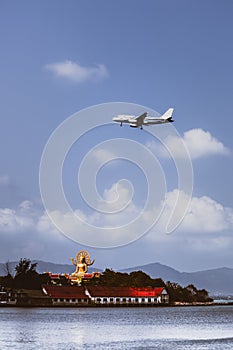 Passenger airplane flying over above big buddha in koh samui island.
