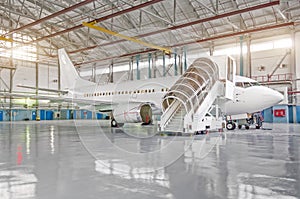 Passenger airplane in the hangar, enclosed engines and gangway at the entrance to the aircraft.