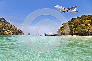 Passenger airplane landing above small island in blue sea and tropical beach