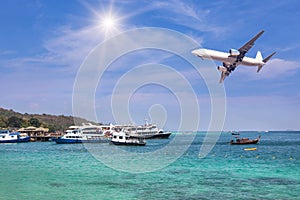 Passenger airplane landing above tropical sea with cruising ships and boats moored in bay.