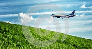 Passenger airplane is landing over a green field. Bright cloudy sky. Panorama