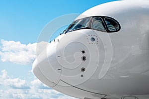 Passenger airplane nose cockpit in blue clouds sky.