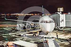 Passenger airplane on runway near the terminal in an airport at night time. Airport land crew doing flight service for passenger a
