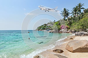 Passenger airplane take off above tropical beach with blue sea on blue sky.