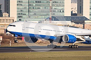 Passenger airplane with two engines landing on runway with touchdown, buildings on background