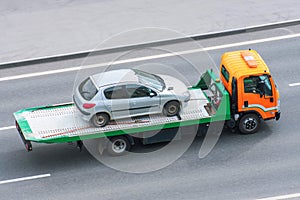 Passenger car in an accident loaded onto an evacuation truck rides along the road and turns onto the highway, aerial side view