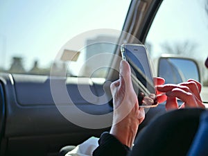 Passenger in car looking at smart phone on the road for navigation while driving.
