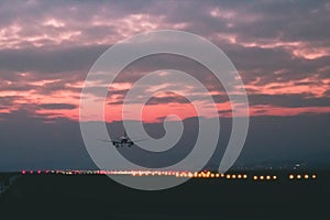 A passenger or cargo plane lands on the runway against the background of red sunset