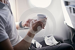 Passenger with face mask drinking coffee in airplane