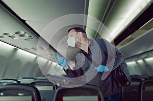 Passenger in face medical mask and blue rubber gloves is finding his seat on a plane