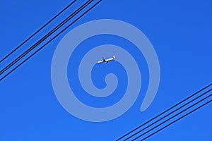 PASSENGER JET IN DEEP BLUE SKY VIEWED BETWEEN OVERHEAD ELECTRICAL CABLES