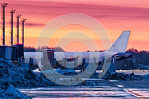 A passenger jet plane stands on the airport apron covered with snowdrifts near a row of aircraft mobile gangway against the