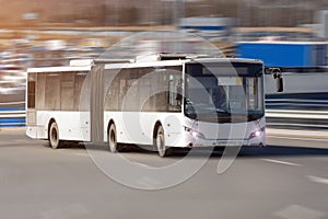 Passenger lengthened articulated bus city bus of white color rides at high speed along the highway. photo