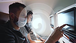 Passenger with masked faces using seatback monitor screen for entertainment.