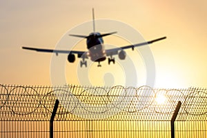 passenger plane landing against the backdrop of the sun and a wire fence