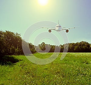 Passenger plane over the field and forest. A bright yellow sun shines