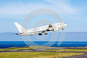 Passenger plane takes off from the airport runway. Ocean at the background.