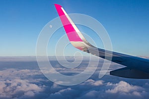 Passenger plane wing in the sky above the clouds. Round moon on the background of blue sky