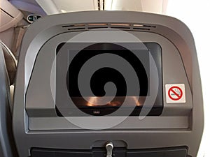Passenger seat of plane with blank empty black monitor screen, and no smoking allowed sign