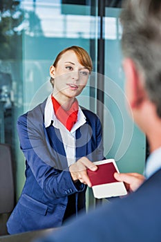 Passenger service agent giving businessman passport and boarding pass in check in area at airport