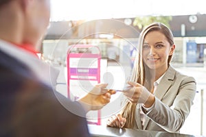 Passenger service agent giving woman`s passport and boarding pass in check in area at airport