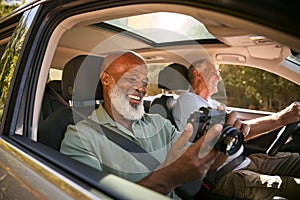 Passenger Taking Photo With Camera As Two Senior Male Friends Enjoy Day Trip Out In Car 