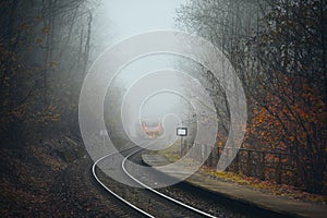 Passenger train leaving railroad station in foggy forest