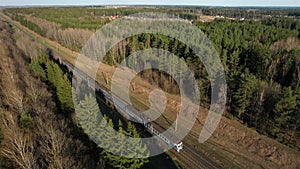 Passenger train on railway from forest, aerial view. Train with passenger cars rides along forests in spring.