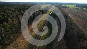 Passenger train on railway from forest, aerial view. Train with passenger cars rides along forests in spring.