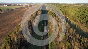 Passenger train on railway from forest, aerial view. Train with passenger cars rides along forests in spring.
