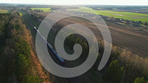 Passenger train on railway from forest, aerial view. Train with passenger cars rides along forests in spring.