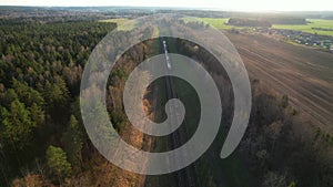 Passenger train on railway from forest, aerial view. Train with passenger cars rides along forests in spring.