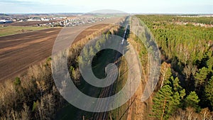 Passenger train on railway from forest, aerial view. Train with passenger cars rides along forests in spring.