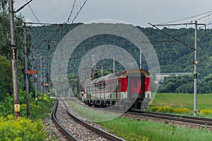 Osobný vlak s červenou elektrickou lokomotívou a osobnými vozňami v lete