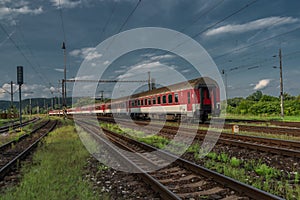 Osobní vlak s červenou elektrickou lokomotivou a osobními vozy v létě