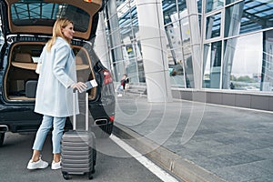 Passenger with travel document and baggage near open car trunk