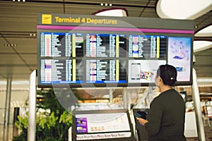 Passenger traveling at the flight information board in airport terminal waiting hall area checking time for departure-arrival and