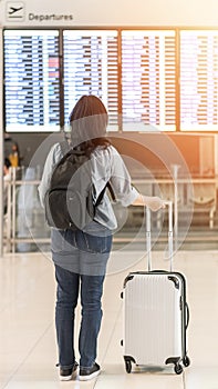 Passenger traveling with luggage and backpack at the flight information board in airport terminal waiting hall area checking time