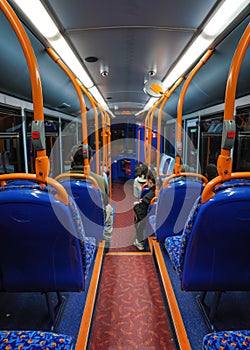 Passenger travelling in otherwise empty public transport bus at evening, view from behind, unoccupied seats visible