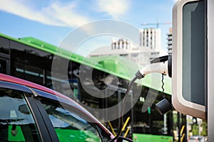 Passenger vehicles are being charged against the background of a passing green bus with passengers