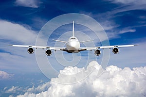 The passenger wide body plane flies high in the blue sky above clouds. Airplane closeup front view