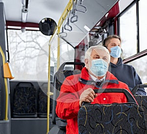 Passengers protecting by medical masks traveling by public transpost, sitting on bus.