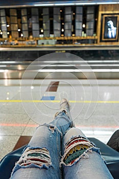 Passengers are waiting for their flight in the airport waiting area. First-person view, girl in ripped jeans